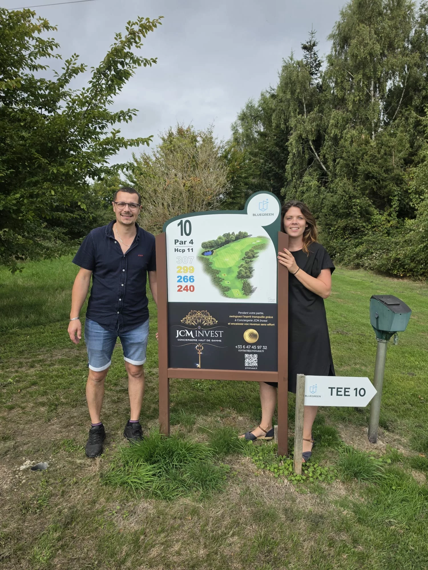 Deux personnes à côté du panneau JCM Invest au départ du trou n° 10 du golf Bluegreen Houlgate